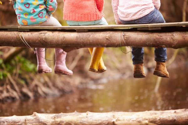 Children sitting on a bridge waving their feet over a river